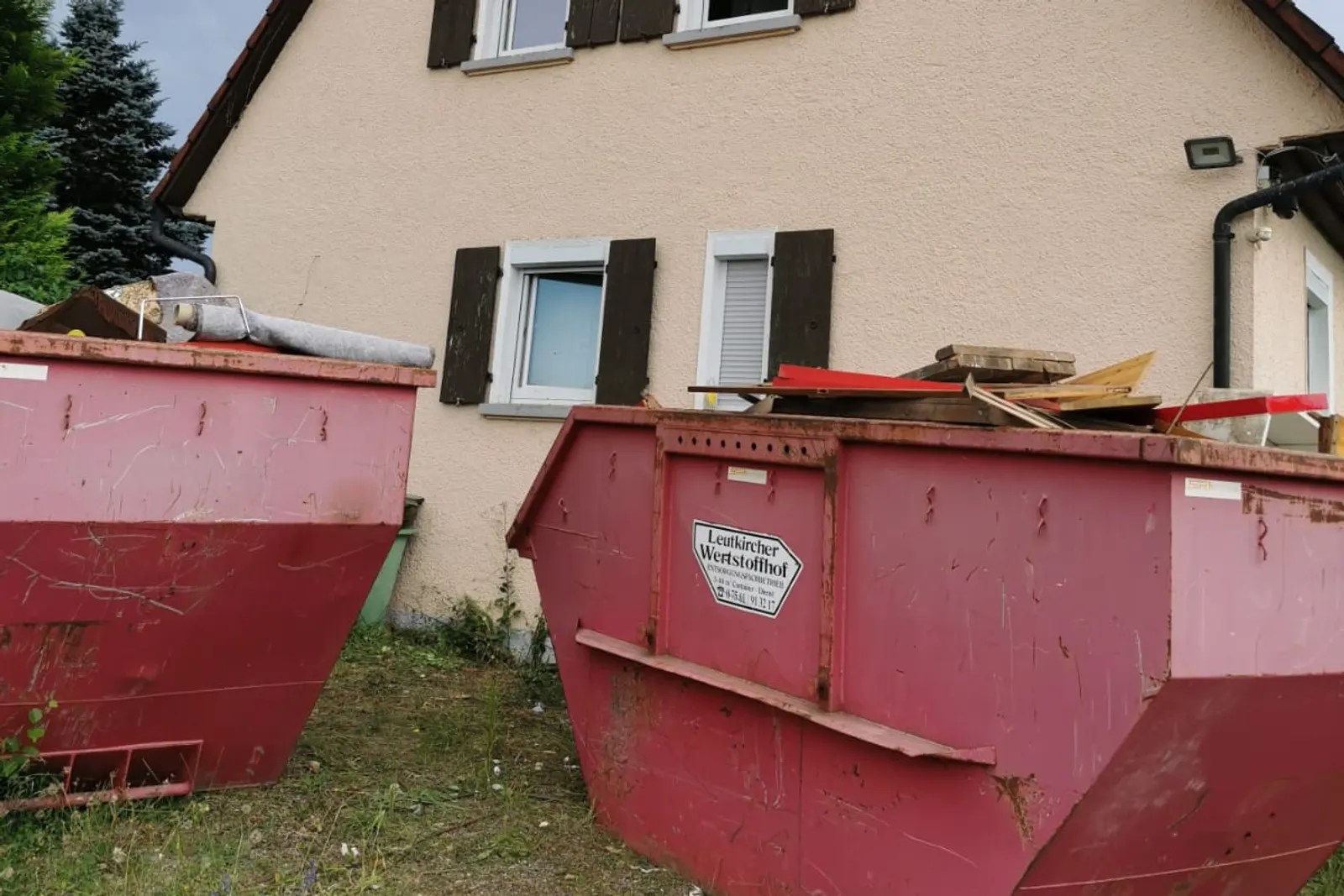 Zwei gefüllte Absetzcontainer mit Sperrmüll vor einem geräumten Wohnhaus