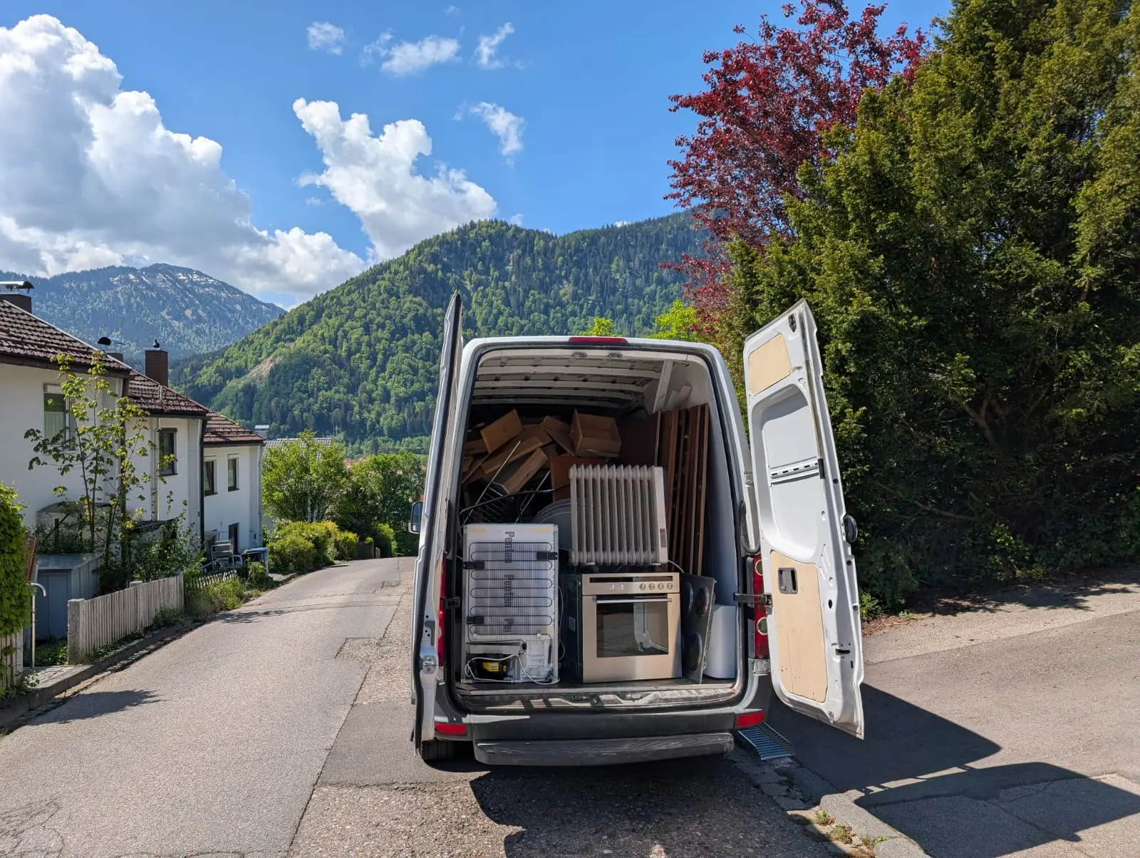 Vollbeladenes Räumfahrzeug mit Möbeln und Elektrogeräten vor Allgäuer Bergkulisse